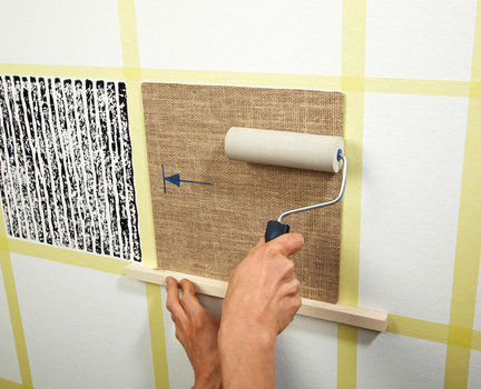 3. Używając kawałka drewna jako podpórki, przytrzymujemy matrycę, aby się nie ześlizgnęła, dociskamy ją do ściany i przesuwamy po niej kilka razy gumowym wałkiem, by dobrze odbić farbę na ścianie.